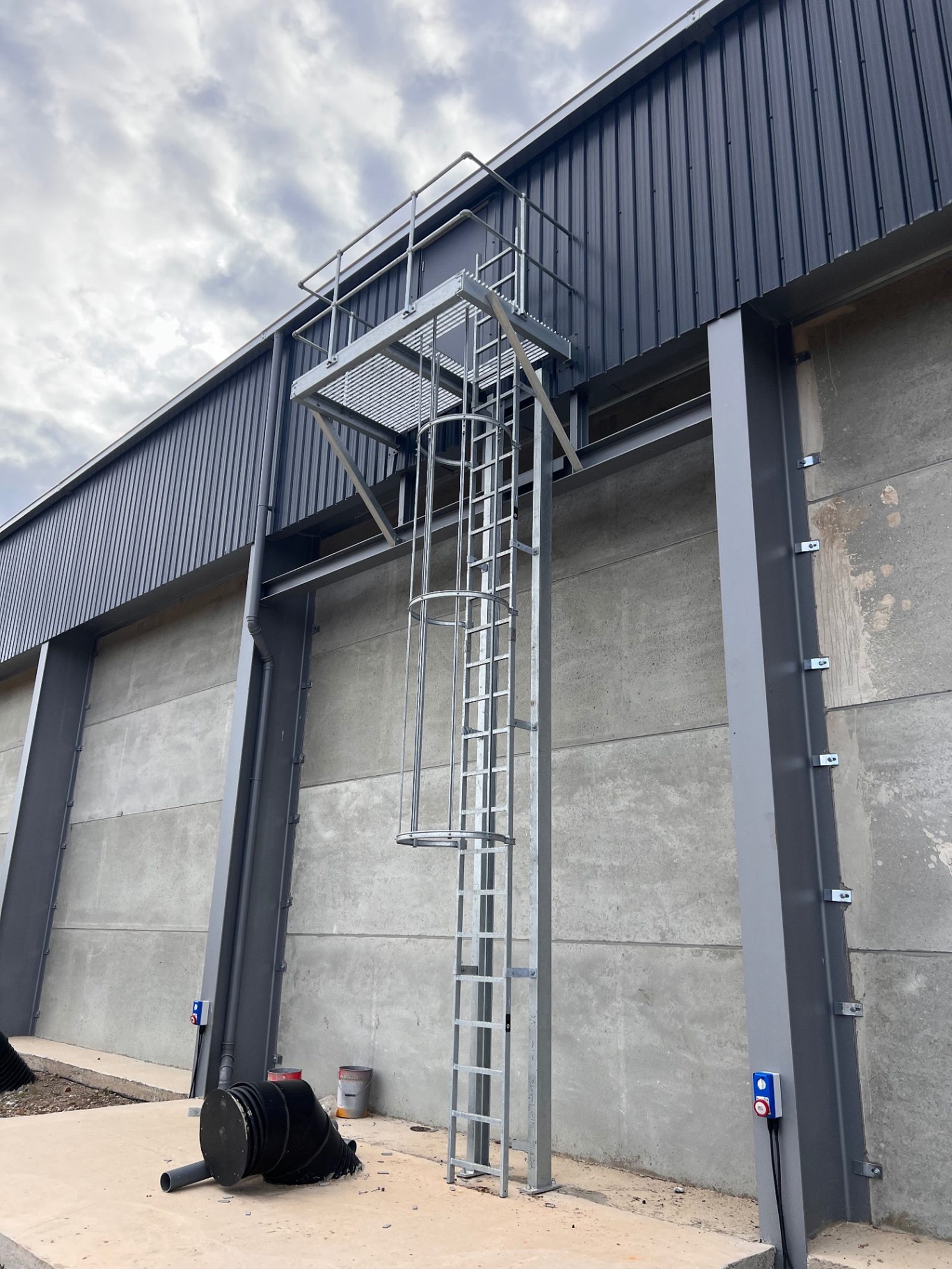 Bespoke galvanised access ladder fabricated by RPD against dark cladding and precast concrete panels on the grain storage building