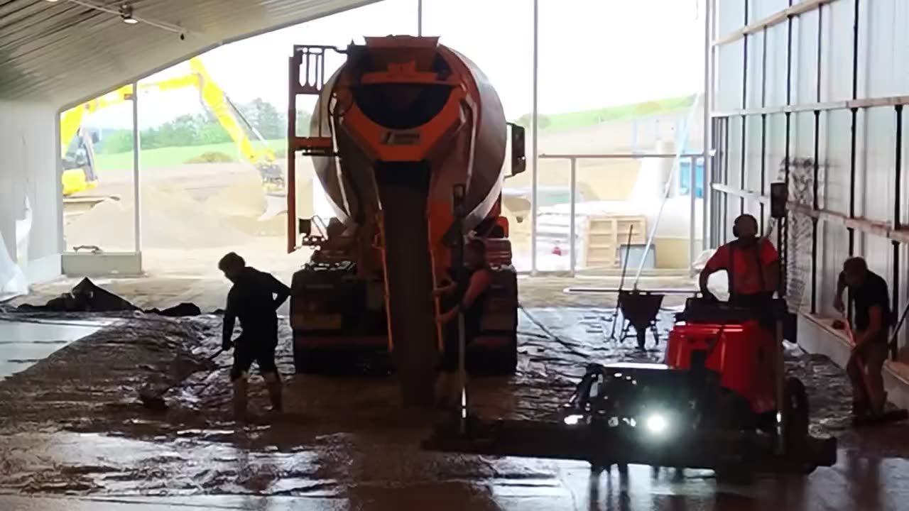 RPD team placing and power-floating a concrete floor slab from a mixer truck inside a steel-framed building