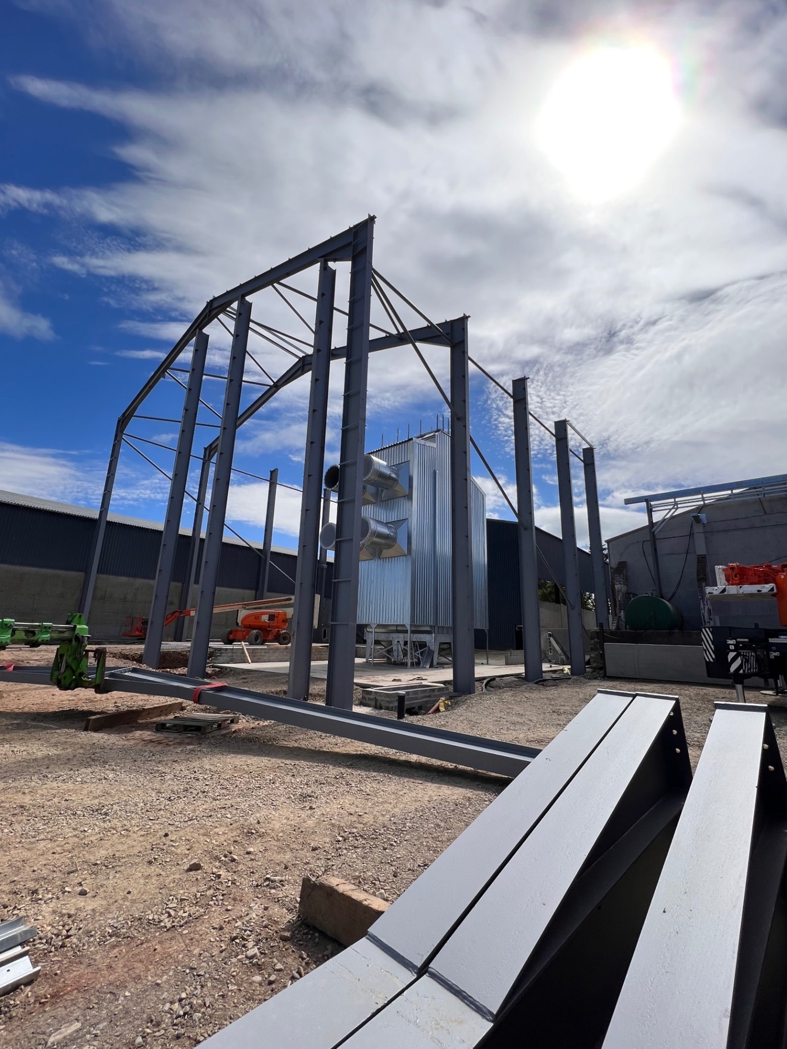 Structural steel frame of the grain storage building against a bright sky during construction